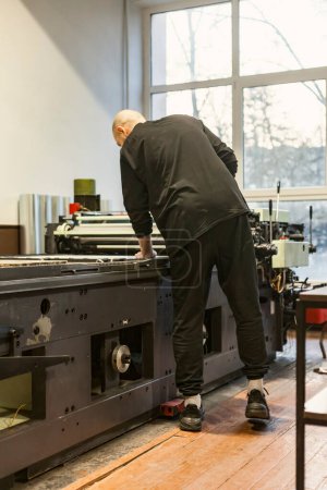 Photo for The artist standing next to a lithographic press, or rolling press in an art workshop. - Royalty Free Image