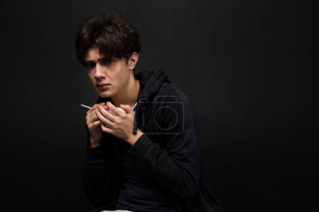 Photo for A homeless young person with bruises under their eyes in dirty, tattered clothing, greedily holding a paper bowl of food. Isolated on black background. - Royalty Free Image