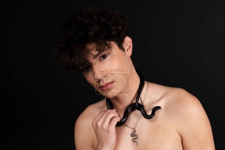 Foto de Joven hombre guapo con el torso desnudo, con una serpiente negra arrastrándose alrededor de su cuello. Aislado sobre fondo negro. - Imagen libre de derechos