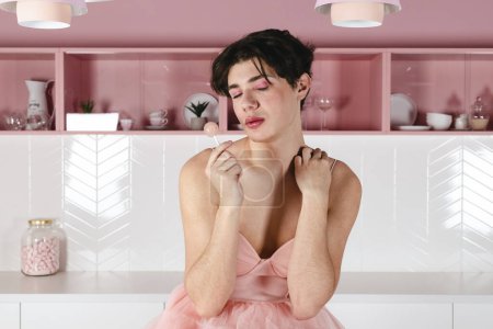 Foto de Retrato de un gay tierno en un vestido rosa con una piruleta. Glamour homosexual joven chico con maquillaje posando en un traje femenino. - Imagen libre de derechos