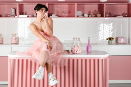 Foto de Retrato de un gay tierno vestido de rosa, bebiendo alcohol. Glamour homosexual joven chico con maquillaje posando en un traje femenino. - Imagen libre de derechos