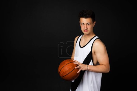 Photo for Minsk, Belarus - May 22nd 2023 - Handsome young basketball player in white sportswear in action with ball, full length. Isolated on black background. - Royalty Free Image