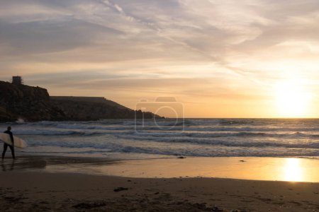Surfer am Strand von Melieha. Sonnenuntergang in der Golden Bay Malta. Sport und Schönheit der Natur.