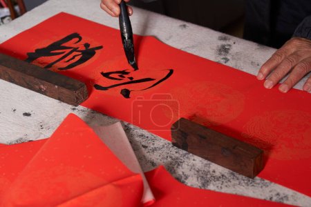 Téléchargez les photos : Un vieux calligraphe écrit des couplets pendant l'Année chinoise du Dragon.Traduction : L'énergie propice apporte auspiciosité et la richesse est abondante. - en image libre de droit
