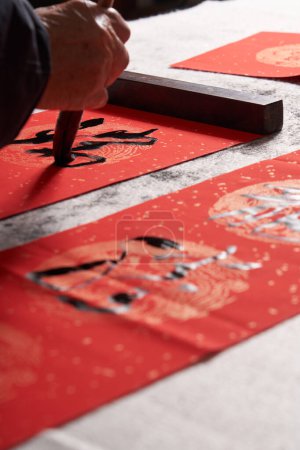 Téléchargez les photos : Un vieux calligraphe écrit des couplets pendant l'Année chinoise du Dragon.Traduction : L'énergie propice apporte auspiciosité et la richesse est abondante. - en image libre de droit