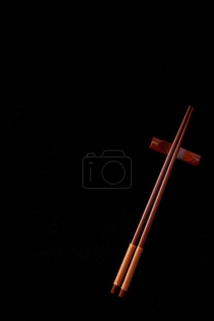 A pair of delicate chopsticks lie on a black background