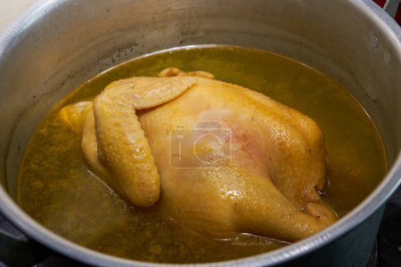 A plump Cantonese white-cut chicken being cooked in the pot