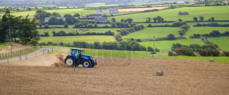 Photo for West Cork, Ireland, August 20, 2022. A tractor sows a plowed field on a summer in Ireland. Agricultural work on an Irish farm, agricultural landscape,  tractor on field. - Royalty Free Image