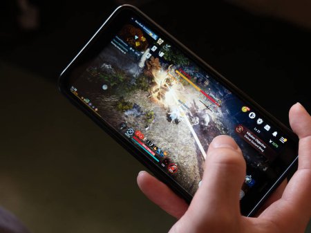 Téléchargez les photos : Cork, Ireland, July 31, 2022. A mobile phone in the hands of a white man. Playing mobile MMORPG Black Desert Mobile. A popular Korean mobile game on a smartphone screen, illustrative editorial. - en image libre de droit