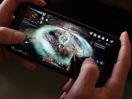 Téléchargez les photos : Cork, Ireland, July 31, 2022. A smartphone in the hands of a white man. Playing mobile MMORPG Black Desert Mobile. A popular Korean mobile game on a smartphone screen, illustrative editorial. - en image libre de droit
