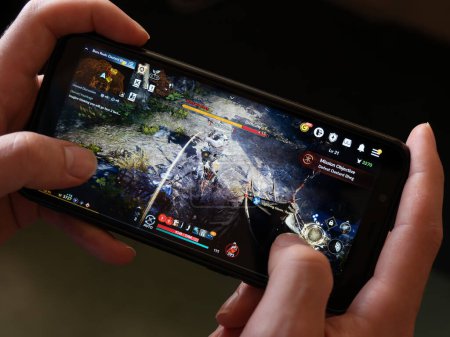 Téléchargez les photos : Cork, Ireland, July 31, 2022. A android phone in the hands of a white man. Playing mobile MMORPG Black Desert Mobile. A Korean mobile game on a smartphone screen, illustrative editorial. - en image libre de droit