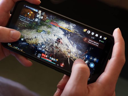 Téléchargez les photos : Cork, Ireland, July 31, 2022. A phone in the hands of a white man. Playing mobile MMORPG Black Desert Mobile. A Korean mobile game on a smartphone screen, illustrative editorial. - en image libre de droit