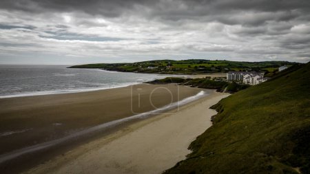 Téléchargez les photos : Plage de sable pittoresque du sud de l'Irlande d'Inchydoney à marée basse par une journée nuageuse, vue sur le dessus. Le littoral de l'île d'Irlande. Belles collines verdoyantes sur l'océan Atlantique. Nuages gris dans le ciel. - en image libre de droit