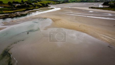 Téléchargez les photos : Plage de sable pittoresque du sud de l'Irlande d'Inchydoney à marée basse par une journée nuageuse, vue sur le dessus. Le littoral de l'île d'Irlande. Belles collines verdoyantes sur l'océan Atlantique. - en image libre de droit