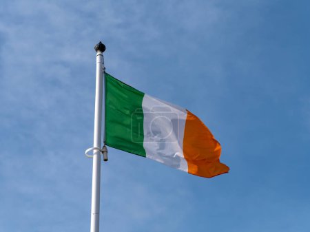 One flag of Ireland on a flagpole against a blue sky.