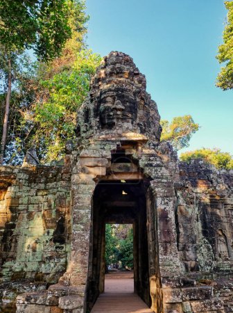 Téléchargez les photos : Photograph showcasing a high stone archway with a tower embellished with carvings of human faces, leading to the old Khmer temple of Banteay Kdei. - en image libre de droit