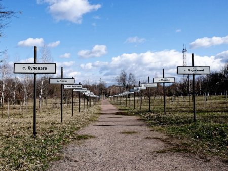 Téléchargez les photos : Un sentier de terre avec des panneaux de chaque côté dans un cadre semblable à un parc. Allée avec les noms des villages abandonnés dans la zone de la catastrophe nucléaire de Tchernobyl. Panneaux avec les noms des villages en cyrillique. - en image libre de droit