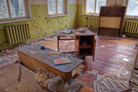Téléchargez les photos : L'image montre une pièce abandonnée avec un bureau, une bibliothèque et un radiateur. Les murs se décollent et le sol est recouvert de débris. Une chambre abandonnée dans la zone d'exclusion de Tchernobyl. - en image libre de droit