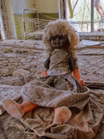 Téléchargez les photos : Une poupée en robe sale est positionnée dans une pièce délabrée. Une vieille poupée avec un visage sale sur un lit dans une maternelle abandonnée. Chambre contaminée par les rayonnements à Tchernobyl. - en image libre de droit