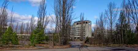 Photo for A dilapidated building with broken windows, surrounded by overgrown vegetation and bare trees. The Polissya hotel is one of the tallest buildings in the abandoned city of Pripyat, Ukraine, Chernobyl. - Royalty Free Image