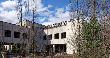 Téléchargez les photos : Un bâtiment délabré avec le mot dessus, entouré d'arbres nus et de végétation envahie. Un restaurant abandonné à Pripyat. Ruines d'un bâtiment dans une ville contaminée par des radiations. - en image libre de droit