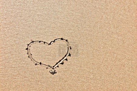 The photo captures a heart outline drawn in sand, highlighting its texture.