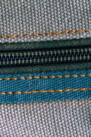 Macro shot of a zipper sewn into woven fabric with visible threads.
