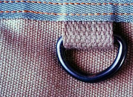 A close-up of a denim fabric edge with a brown, textured loop attached, lying on a woven surface.