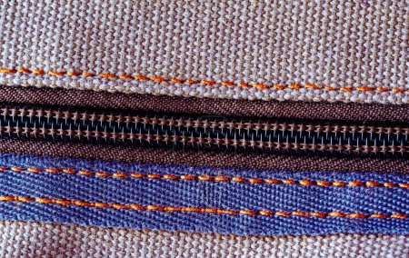 Detailed view of a zipper on brown textured fabric, highlighting the stitches.