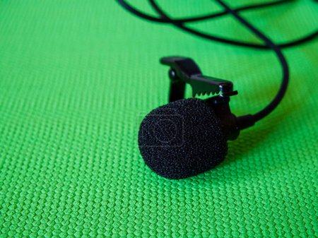 Audio Recording Gear. Kabelgebundenes Revers-Mikrofon mit Clip vor grün strukturierter Oberfläche.
