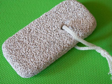 Photo for Pumice Stone on Green. A grey pumice stone with a white string on a green background, showing its porous surface. - Royalty Free Image