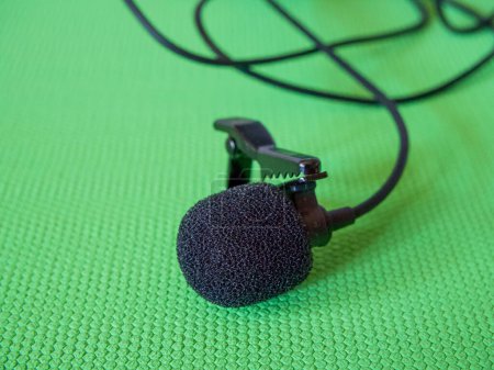 Lavalier Mikrofon Detail. Ein schwarzes Lavalier-Mikrofon mit Schaumstoff-Windschutzscheibe und Clip auf grünem Hintergrund.
