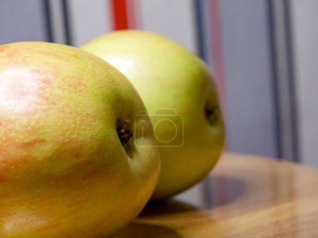 Green Apples on Wood. Two green apples with a red blush on a wooden surface against a striped backdrop, depicting freshness and health.