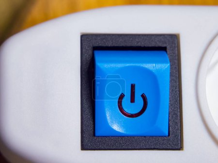 Ein blauer Einschaltknopf mit einem Power-Symbol, das auf einem weißen Gerät angebracht ist und auf Funktionalität hindeutet.