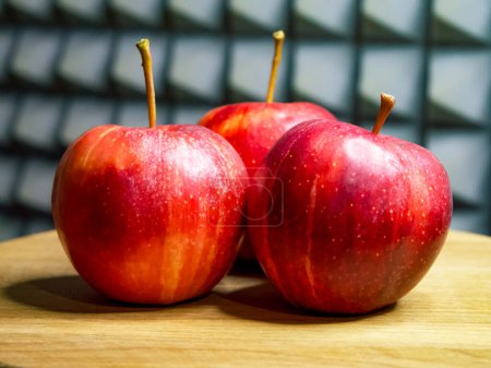 Pommes fraîches exposées. Trois pommes rouges avec des tiges sur une surface en bois.