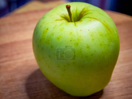 Ein grüner Apfel mit Stiel auf einer Holzoberfläche, der Frische und Gesundheit anzeigt.