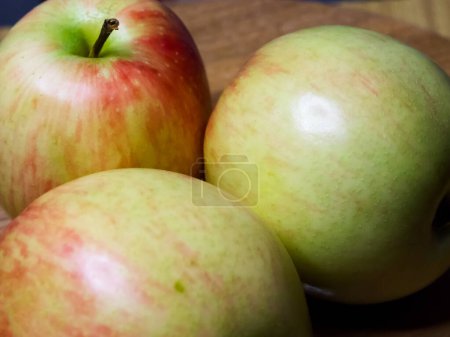 Frisches Apple Trio. Drei rote und grüne Äpfel auf einer Holzoberfläche, die natürliche Frische vermitteln.