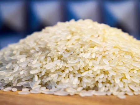 Ein Haufen ungekochter weißer Reiskörner auf einer hölzernen Oberfläche, hell und sauber, geeignet für kulinarische Themen.
