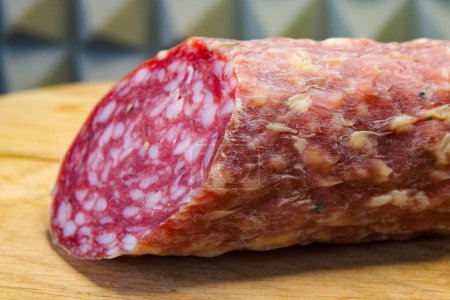 A piece of salami on a wooden board, highlighting its texture and suitability for culinary content.