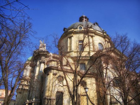 Winters Architecture: A domed historic building framed by leafless trees under a bright blue sky, suggesting winter. The Dominican church and monastery in Lviv, Ukraine