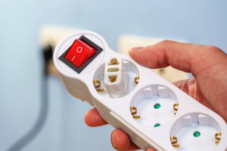 Foto de Adaptador de enchufe conectado en un divisor eléctrico con enchufes europeos y un botón de interruptor rojo en la mano - Imagen libre de derechos