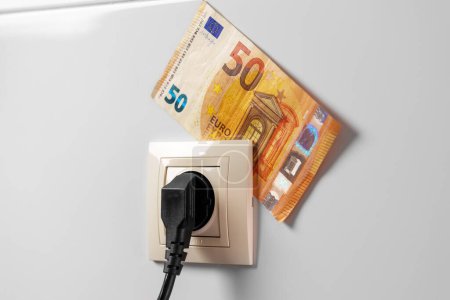Konzeptionelle Ansicht von Eurogeld und Haushaltssteckdose mit Stecker aus nächster Nähe. Effizienz- und Energiesparkonzept