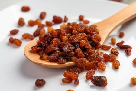 Dehydrated sweet sundried raisins in wooden spoon closeup