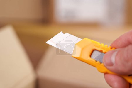 Foto de Cuchillo utilitario o cortador de caja en mano con cuchilla segmentada retráctil para unboxing de paquete de cerca - Imagen libre de derechos