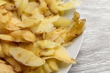 Foto de Cáscara de patata en plato de cocina blanco. Desperdicio de alimentos de cerca - Imagen libre de derechos