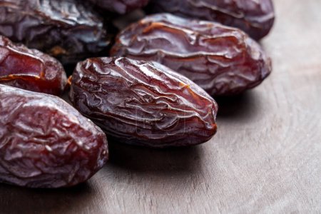 Sweet organic Medjool dates with wrinkled peel on a brown wooden surface. Macro