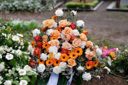 Téléchargez les photos : Fleurs funéraires élégantes d'oeillets blancs, gerbera orange et roses rouges et roses sur une tombe après un enterrement - en image libre de droit