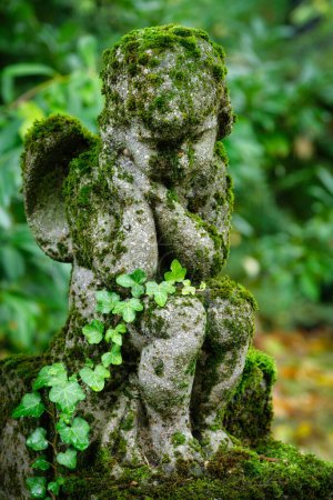 moss covered small putto sitting tired on a stone at a grave in a cemetery