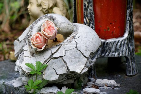 ein zerbröselndes Steinherz mit Rosen auf einem verlassenen Grab auf einem Friedhof