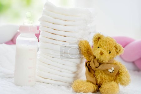 Photo for Baby diapers stack cute teddy bear sitting next, white color bed. Newborn nappies concept - Royalty Free Image